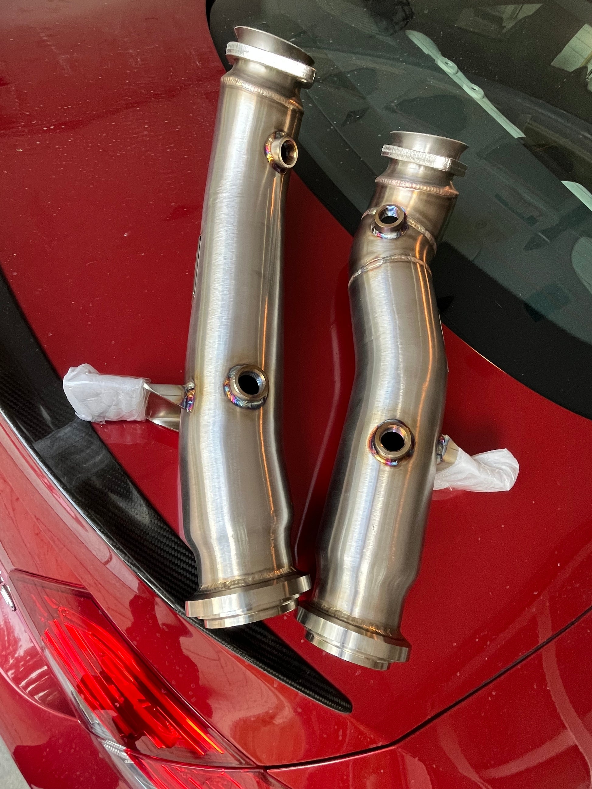 Pair of stainless steel downpipes displayed on vehicle surface for Mercedes AMG M276