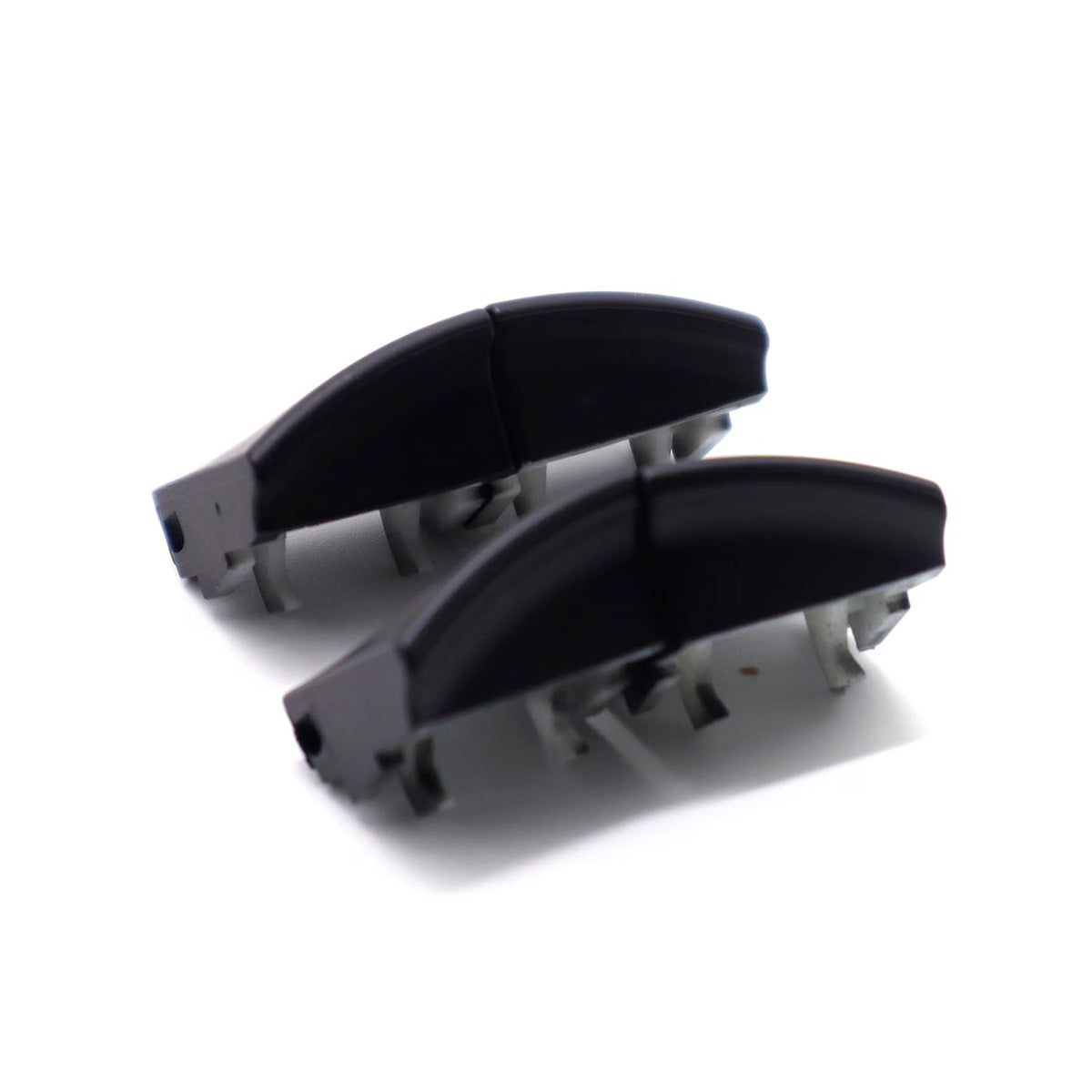 Two black window switch button caps laid out and viewed from the side, showing the curved profile and mounting clips